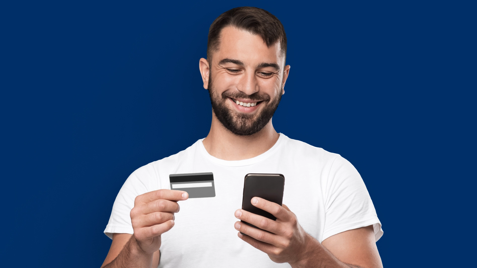Imagem mostra homem sorrindo ao utilizar celular e cartão de crédito