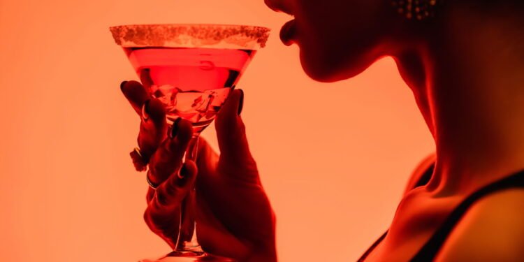 Visão recortada de uma mulher bebendo um coquetel margarita sobre fundo laranja - depositphotos.com / VitalikRadko7