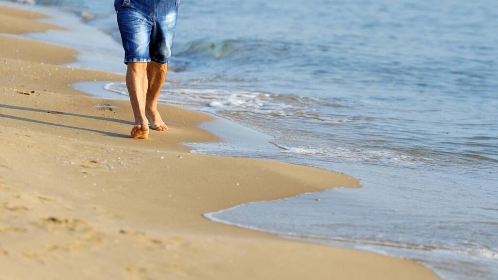 Pessoa caminhando em areia fofa de praia para fortalecer as articulações