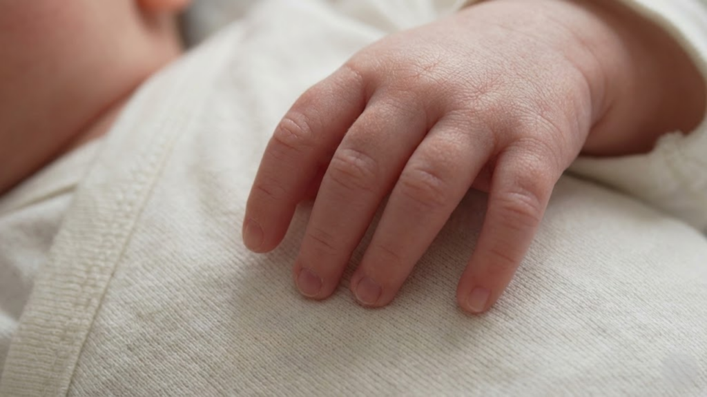 Close macro da mão delicada de um recém-nascido tocando um tecido de algodão, destacando a sensibilidade da pele