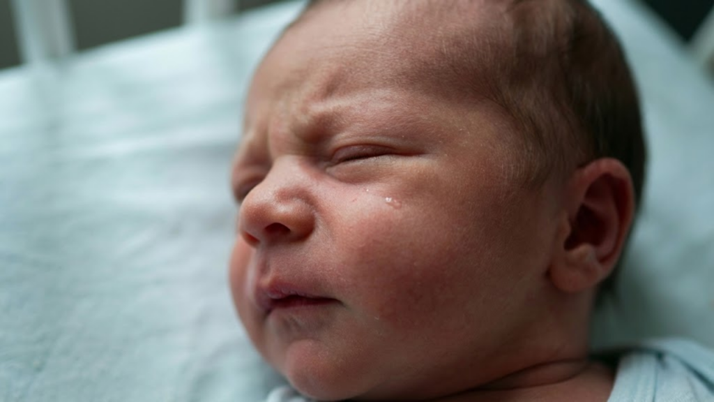 Close extremo do rosto de um recém-nascido desviando o olhar e franzindo a testa, demonstrando sobrecarga sensorial