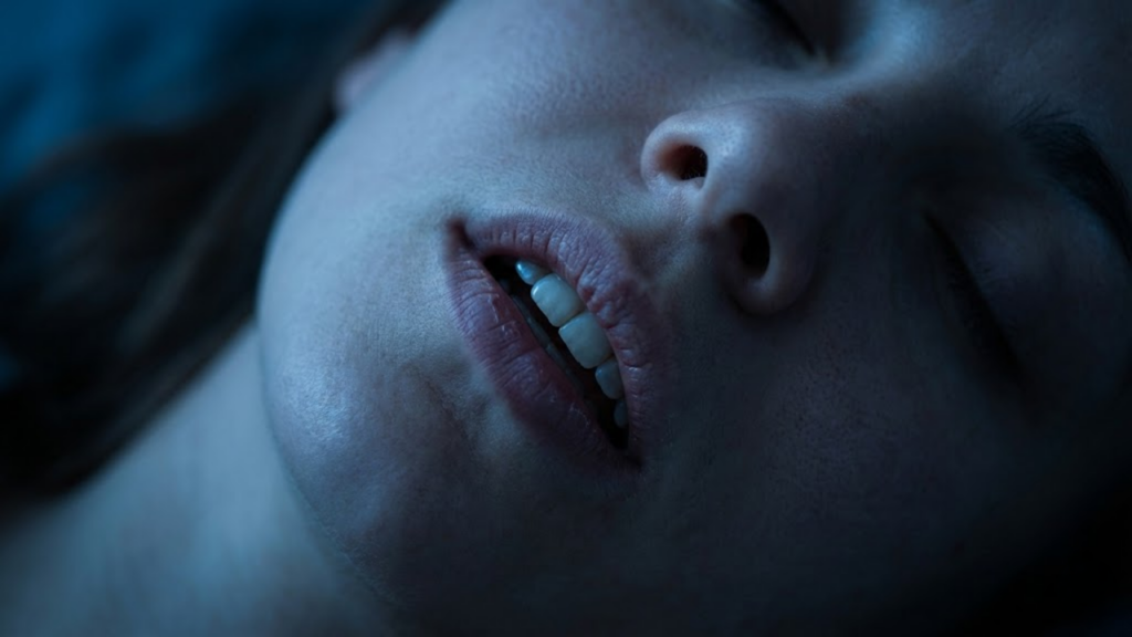 Close noturno de uma mulher dormindo de boca aberta, com foco nos lábios e dentes secos sob luz lunar