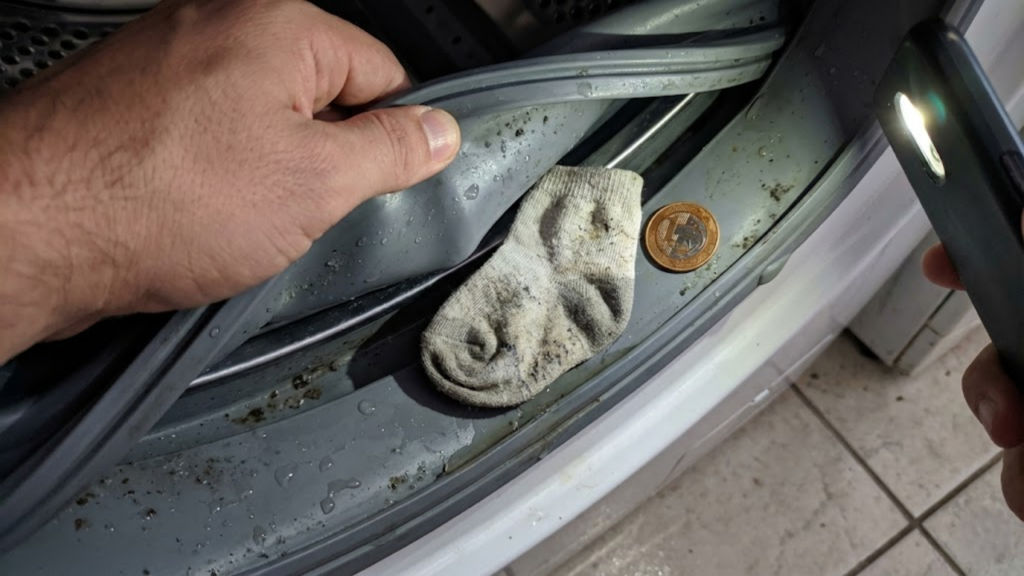 Peças de vestuário presas nos componentes mecânicos internos de uma lavadora automática de roupas