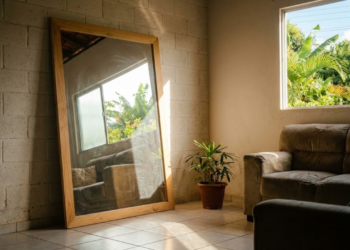 Espelho posicionado na parede oposta à janela refletindo luz solar para o interior do ambiente
