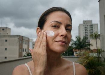 Mulher brasileira sob céu nublado aplicando protetor com confiança