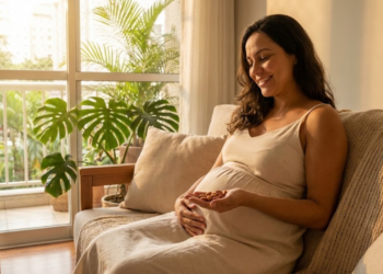 Grávida sorrindo aliviada no sofá, segurando amêndoas cruas com luz do sol