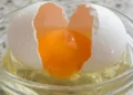 Macro detalhado de um ovo sendo quebrado, destacando a cor vibrante da gema e a textura da clara.