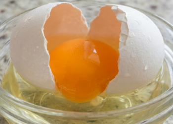 Macro detalhado de um ovo sendo quebrado, destacando a cor vibrante da gema e a textura da clara.