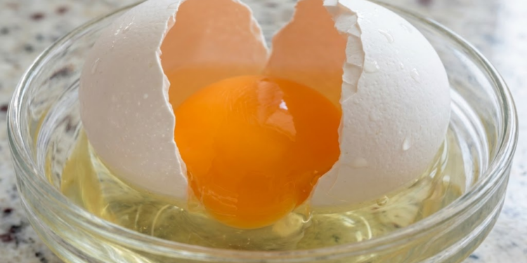 Macro detalhado de um ovo sendo quebrado, destacando a cor vibrante da gema e a textura da clara.