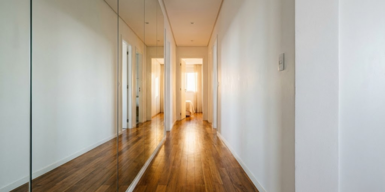 Corredor iluminado com espelho lateral duplicando a largura do chão