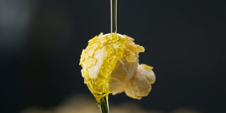 Close macro de um fio de azeite caindo sobre um grão de pipoca crocante.