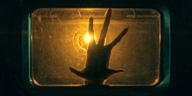 Mão pressionada contra uma janela iluminada por luz dourada em cena da série The Boroughs, da Netflix