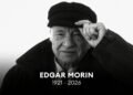 Retrato em preto e branco do filósofo Edgar Morin usando uma boina e tocando a aba com a mão esquerda. Na parte inferior, há o texto centralizado "EDGAR MORIN 1921 - 2026" em letras brancas sobre fundo escuro.