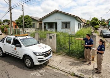 Fiscais da prefeitura inspecionando jardim com grama alta em residência durante operação de fiscalização urbana.