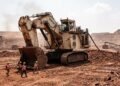 Escavadeira hidráulica gigante de mineração em tons creme conectada a cabo elétrico em mina a céu aberto, com operários ao lado mostrando a escala
