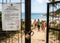 Portão de acesso a praia mantido aberto com documento judicial fixado garantindo a circulação pública.