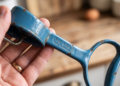Mão segurando utensílio de cozinha vintage de metal azul com inscrição "THE KING MADE IN BRAZIL", apresentando marcas de desgaste e ferrugem.