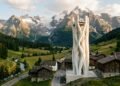 Torre branca impressa em 3D de 30 metros erguendo-se acima dos telhados de pequena vila alpina na Suíça com montanhas ao fundo