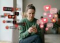 Jovem mãe com celular cercada por balões de comentários críticos e de apoio nas redes sociais.