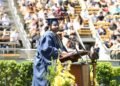Homem maduro de beca e capelo segura medalha de honraria em cerimônia de formatura, emocionado.
