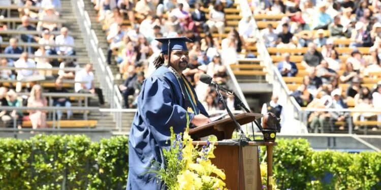 Homem maduro de beca e capelo segura medalha de honraria em cerimônia de formatura, emocionado.