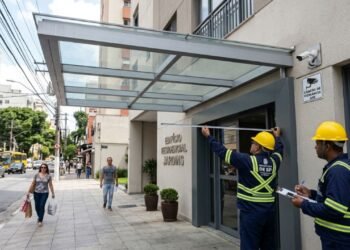 Edifício residencial constrói marquise de vidro e alumínio que se projeta 1,5 metro além do limite do lote sobre a calçada pública sem autorização da Secretaria de Obras; a fiscalização autua o condomínio por invasão de espaço aéreo público e exige a readequação do projeto.