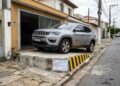 Morador constrói rampa de concreto na calçada para facilitar o acesso de SUV à garagem, criando um degrau de 25 cm no passeio público que provoca quedas de pedestres e impede o trânsito de cadeirantes; a prefeitura aplica multa por infração ao Código de Posturas e exige a demolição da estrutura