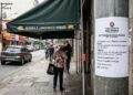 Comerciante instala estrutura pesada de metal e lona para cobertura de fachada fixa a apenas 1,80 m do chão na calçada, forçando pedestres de maior estatura a se abaixarem ou irem para a rua; a prefeitura emite auto de infração exigindo o rebaixamento ou elevação da estrutura ao limite mínimo de 2,50 m.