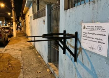 Morador fixa suporte metálico de lixeira com hastes pontiagudas projetadas para fora da linha do lote na altura da cabeça dos pedestres, provocando acidentes com pessoas que caminham à noite; a prefeitura autua o responsável por colocação de obstáculo perigoso em área pública