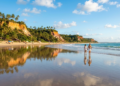 A praia onde o mar vira espelho na maré baixa, com piscinas naturais entre recifes, falésias vermelhas e Mata Atlântica protegida