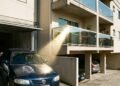 Morador instala fechamento de varanda com vidros espelhados para bloquear o sol, o reflexo concentrado queima a pintura do carro do vizinho parado na garagem ao lado e a disputa vai parar no Juizado Especial Cível