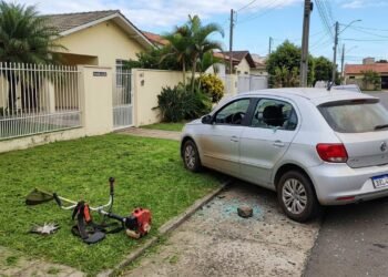 Vizinho corta grama e pedra lançada pela roçadeira quebra vidro do carro estacionado ao lado; ninguém viu o momento exato do impacto