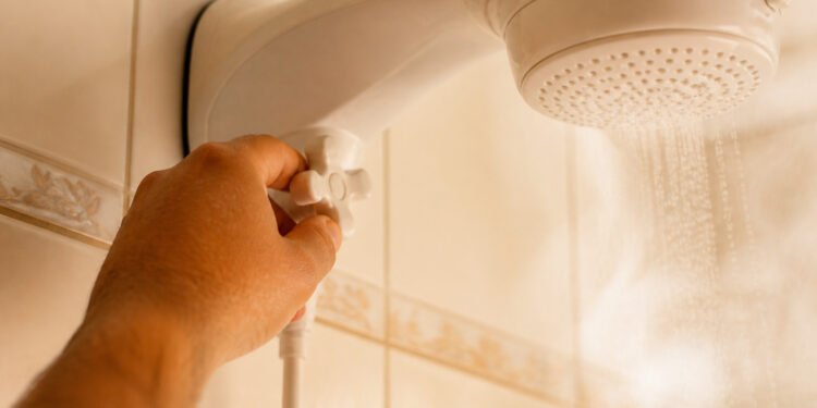 Mão abre o registro antes de ligar o chuveiro