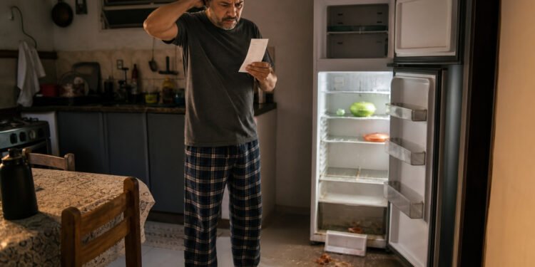 Homem diante de geladeira quebrada com nota fiscal na mão