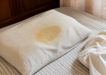 Travesseiro com mancha amarelada no centro sobre a cama sem roupa