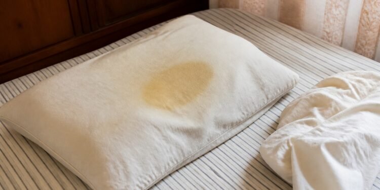 Travesseiro com mancha amarelada no centro sobre a cama sem roupa
