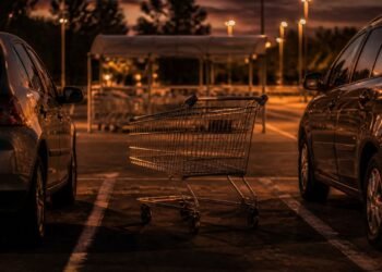 Carrinho abandonado entre carros no estacionamento do mercado ao anoitecer