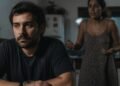 Homem em silêncio à mesa da cozinha enquanto a conversa continua