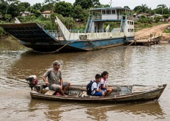 Pescador atravessa um rio diariamente em uma embarcação improvisada para levar os filhos à escola e descobre que uma balsa comprada por R$ 740 mil permanece parada há 14 meses; o município afirma que o transporte ainda depende de regularização para começar a operar