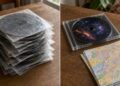 Cópias de CD em envelopes de papel ao lado do disco original com estojo e mapa