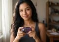 Jovem segura câmera digital compacta violeta perto da janela