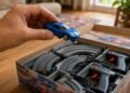 Dedos seguram carrinho azul de autorama sobre caixa com pista completa