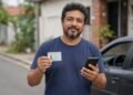 Motorista segura carteira de habilitação e celular ao lado do carro