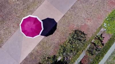 18/08/2017. Crédito: Breno Fortes/CB/D.A Press. Brasil. Brasília - DF. Foto aérea de uma pessoa andando com guarda-chuva sob o sol.